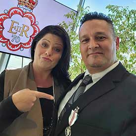 Earl Thiessen wearing a suit with a woman standing next to him and pointing to an award on his lapel.