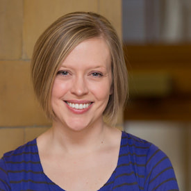 Natalie is smiling to the camera. She is wearing a dark blue shirt, short-cutted hair with blonde and black color.